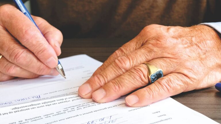 Older signer signing a document, close up